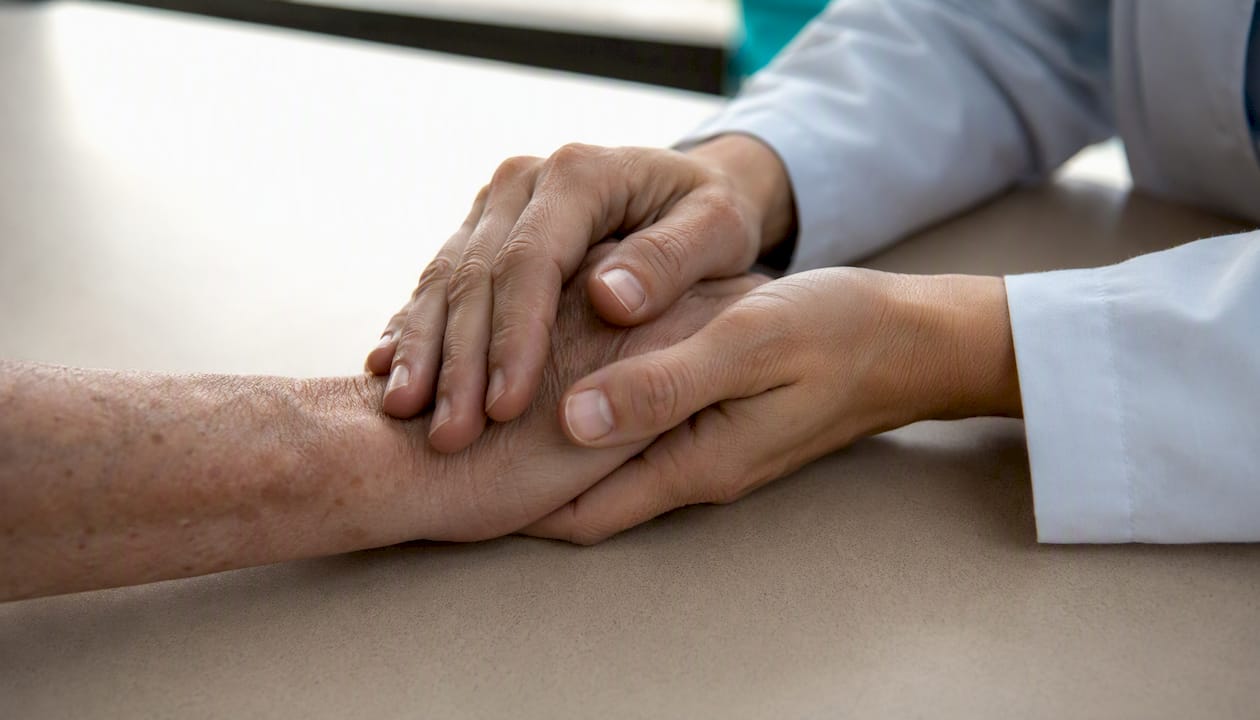 Des mains délicates qui accompagnent avec douceur celle du patient.